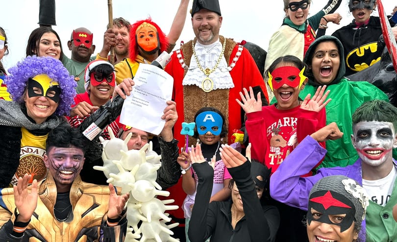 Swimmers in fancy dress crowded around the Mayor of Tenby in red robes and chain of office, holding up a fancy dress certificate.