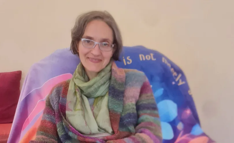 Catriona smiles from an armchair draped in a colourful throw, a patterned cushion on her lap.