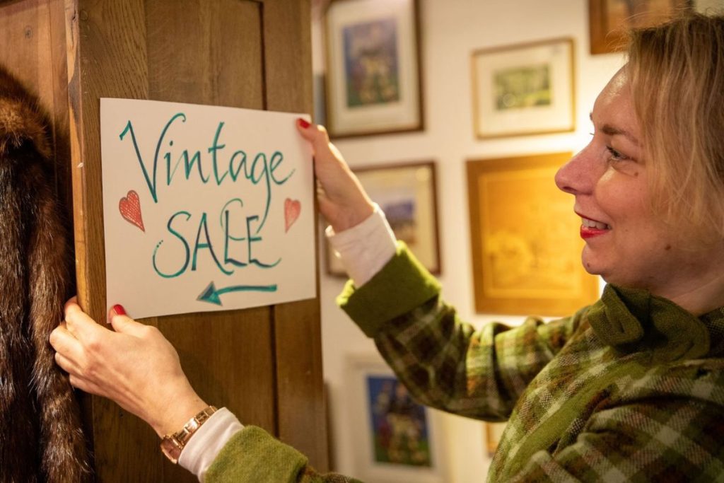A volunteer retail assistant hangs up a sign: "vintage sale".